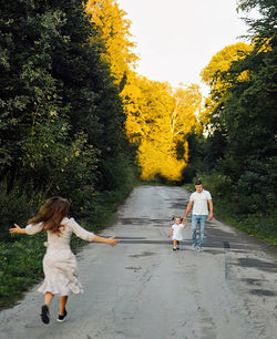 Woman with arms flung open runs to greet husband and young daughter on a country road