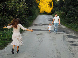 Woman with arms flung open runs to greet husband and young daughter on a country road