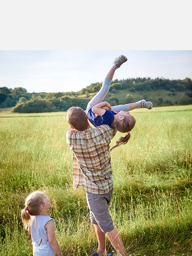 Father playing with daughters in a tall grass field