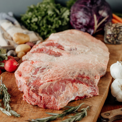 Raw Large Beef Brisket raw on a wooden cutting board with vegetables and herbs.