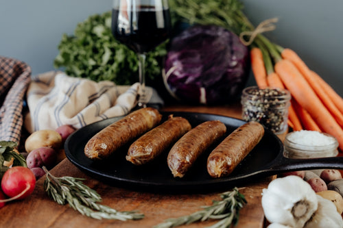 A platter of four beef Italian sausage links cooked with a variety of vegetables on a wooden table