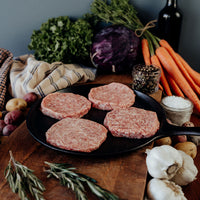 Raw Pork Burger Patties on a pan with vegetables and herbs on a wooden surface