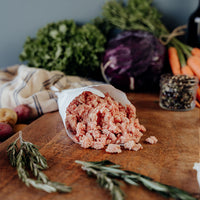Raw Ground Pork in a paper cone on a wooden cutting board with vegetables and herbs.