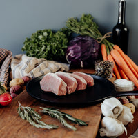 Four raw Boneless Pork Chops on a cutting board with vegetables and a bottle of wine on a wooden table.