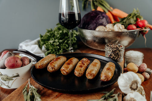 Cooked Chicken Apple Sausage on a black plate with vegetables and a glass in the background