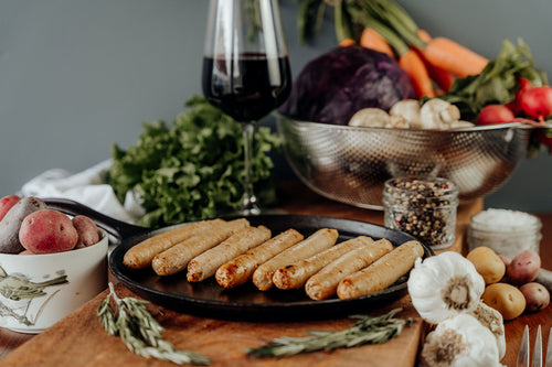 Cooked Chicken Sausage Links on a black plate with vegetables and a bottle in the background