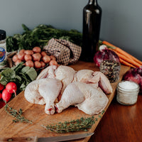 Raw Spatchcock Whole Chicken on a wooden cutting board with vegetables, a bottle of wine, and herbs on a wooden table.