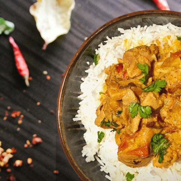Bowl of curry with rice on a dark surface with red chili peppers.