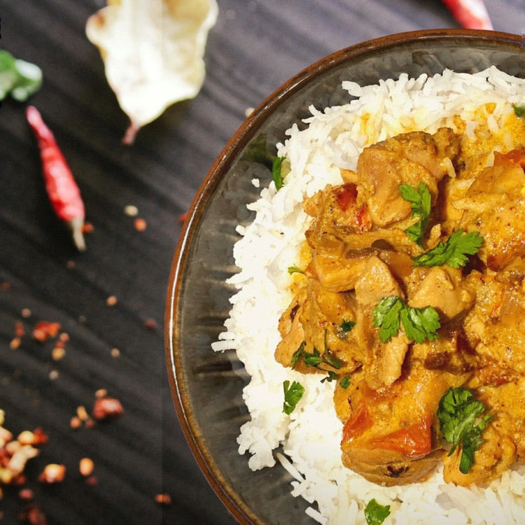 Bowl of curry with rice on a dark surface with red chili peppers.