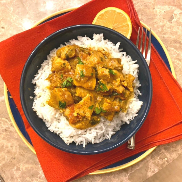 Bowl of chicken curry over rice on a red napkin with a lemon wedge.