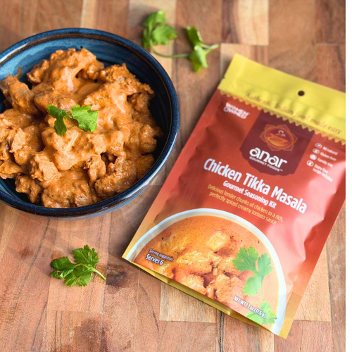 Bowl of Chicken Tikka Masala with an Anar Chicken Tikka Masala seasoning packet on a wooden surface.