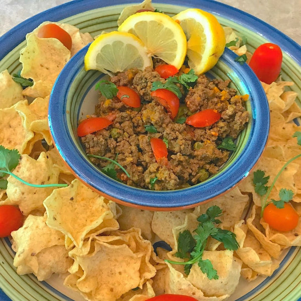 Dip with ground meat and vegetables surrounded by tortilla chips on a decorative plate.