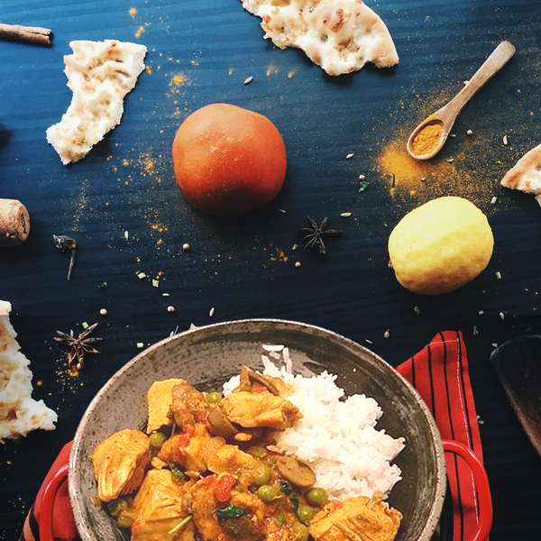 Curd rice with chicken and peas in a bowl on a dark surface with spices and bread.