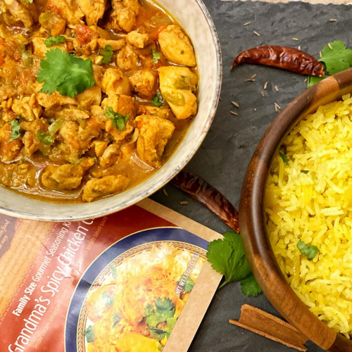 Bowl of chicken curry with a side of yellow rice on a dark surface, featuring a recipe book.