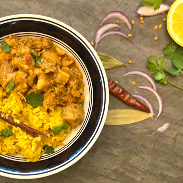 Bowl of curry with rice on a dark surface with garnishes