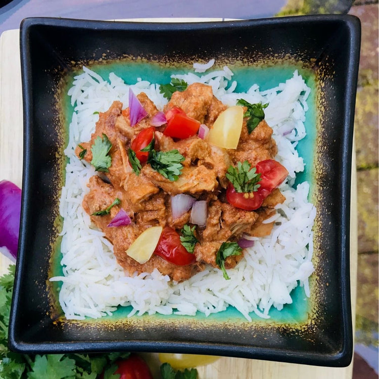 Plated dish of rice with curry and vegetables on a black square plate.