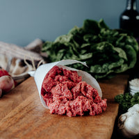 Ground bison on a wooden cutting board with vegetables in the background