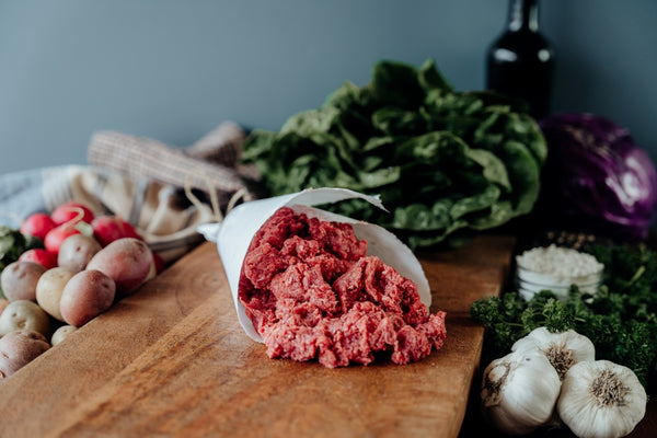 Ground bison on a wooden cutting board with vegetables in the background