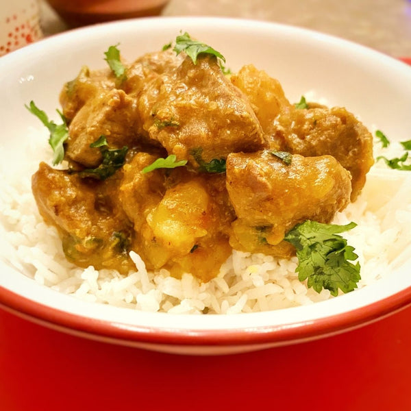 Curried chicken over rice in a white bowl with a red rim