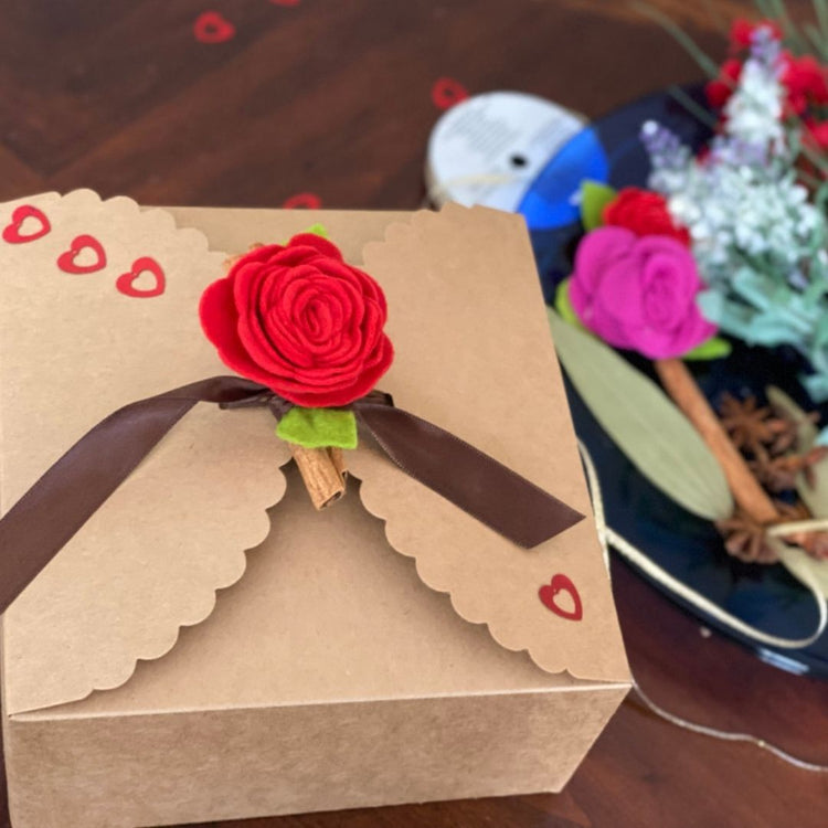 Brown gift box with a red rose and brown ribbon on a wooden surface.