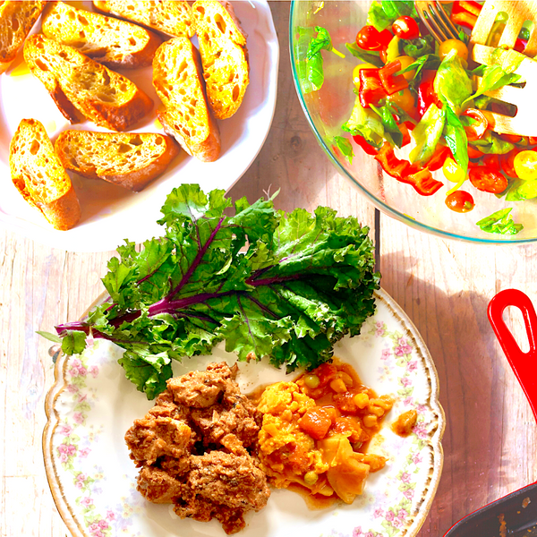 Dish with greens, scrambled eggs, and meatballs on a wooden table with bread and salad in the background.