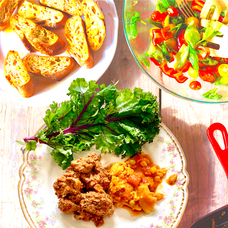 Dish with greens, scrambled eggs, and meatballs on a wooden table with bread and salad in the background.