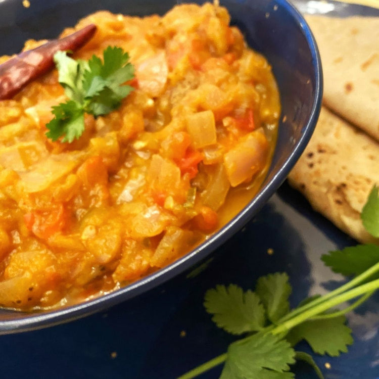 Bowl of orange curry with naan bread on a blue plate