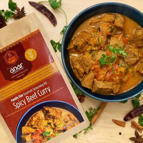 Anar Spicy Beef Curry seasoning kit beside a bowl of curry on a wooden surface.