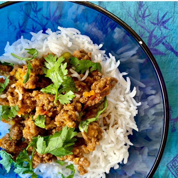 Mince meat with vegetables over rice in a blue bowl on a textured blue background