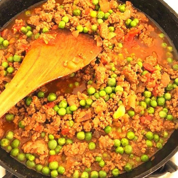 Stir-fry dish with ground meat and peas in a pan with a wooden spatula.