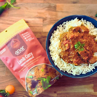 Bowl of lamb curry with rice next to a 'lanor' lamb curry seasoning kit on a wooden surface.