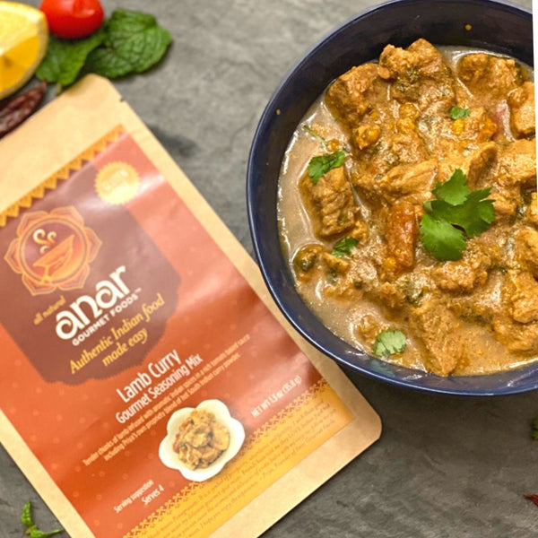 Anar Lamb Curry seasoning kit beside a bowl of curry on a dark surface.
