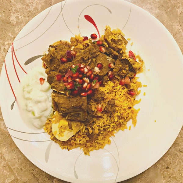 Plated dish of yellow rice with meat and pomegranate seeds on a decorative plate.
