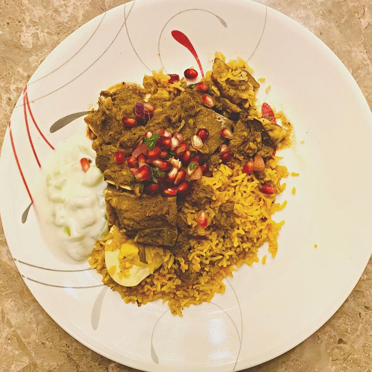 Plated dish of yellow rice with meat and pomegranate seeds on a decorative plate.