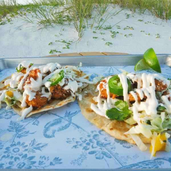 Wild-caught Shrimp Tacos with toppings on a tray by the beach