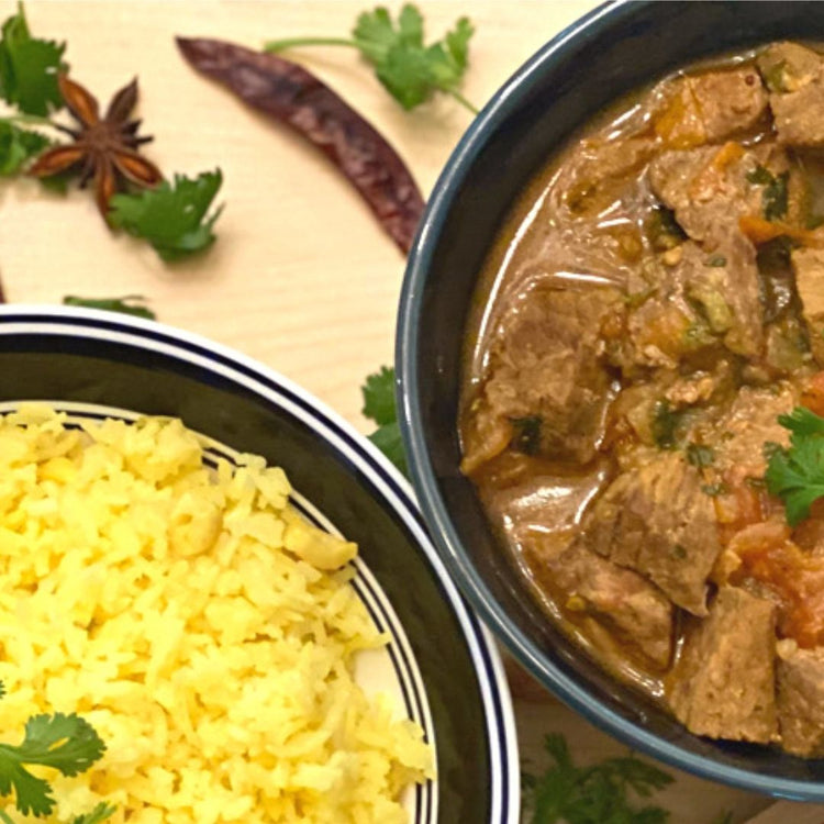 Two bowls of food with yellow rice and a meat dish on a beige background with spices.