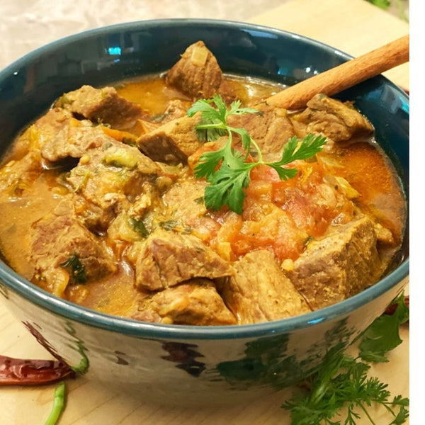 Bowl of beef stew with a wooden spoon on a wooden surface