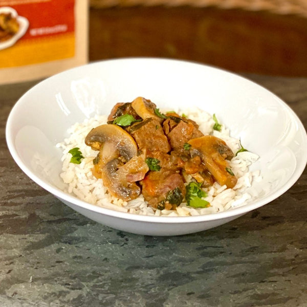 Bowl of food with rice, mushrooms and greens on a white plate