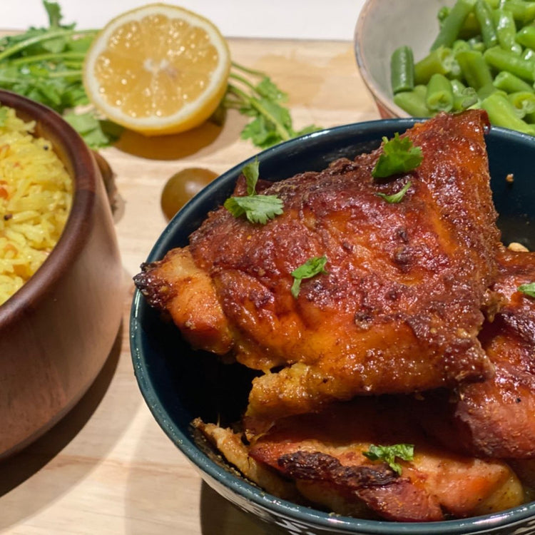 Bowl of fried chicken with sides of rice, green beans, and lemon on a wooden table.