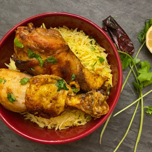 Bowl of yellow rice with roasted chicken drumsticks on a dark surface.