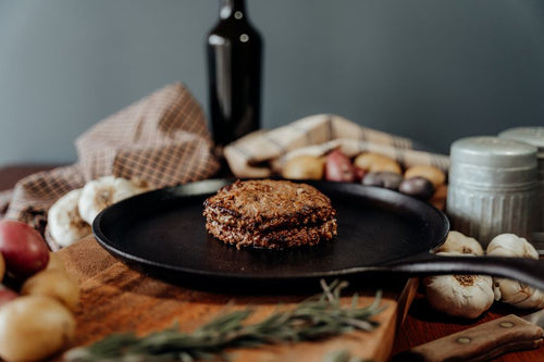 Stack of two cooked 55 lean beef ground patties on a black plate with garlic and potatoes in the background.