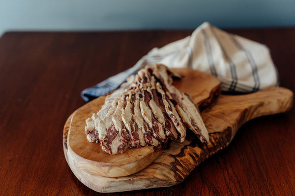 Wooden cutting board with raw sliced Sugar-Free Beef bacon on a wooden surface with cloth in the background