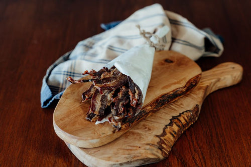 Wooden cutting board with cooked sliced Sugar-Free Beef bacon wrapped in a cloth on a wooden surface 