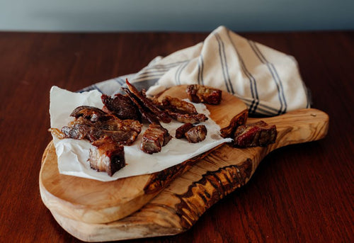 Raw Sugar-Free Beef Bacon Tips on a wooden cutting board with a cloth in the background