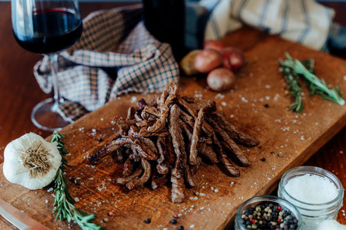 Cooked Grass-Fed Stir Fry Beef on a wooden cutting board with rosemary, potatoes, garlic, and a glass of wine