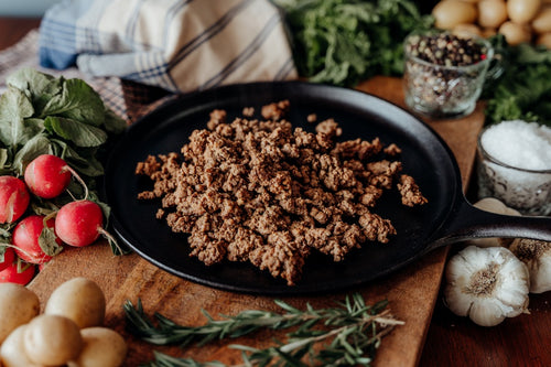 Cooked 55% Lean Beef, Ground with Beef Heart, Organ Blend Burger, High Fat Keto Burger on a black plate with a variety of vegetables and spices with a towel in the background