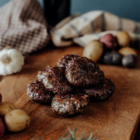 Cooked Grassfed Adobo Beef Meatballs on a wooden cutting board with garlic and other vegetables in the background