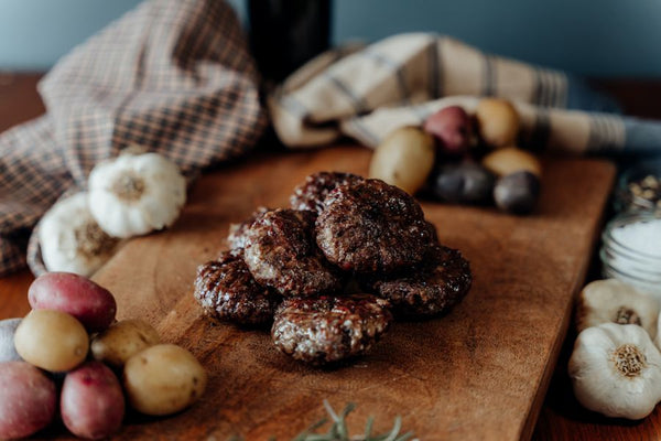 Cooked Grassfed Adobo Beef Meatballs on a wooden cutting board with garlic and other vegetables in the background