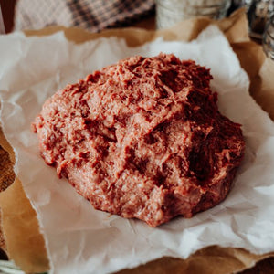 Raw 75% Lean Ground Beef with Heart, Kidney, Liver blend on a piece of paper with a wooden surface in the background