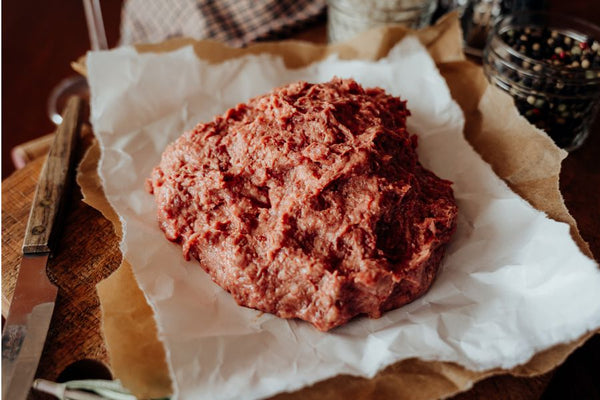Raw 75% Lean Ground Beef with Heart, Kidney, Liver blend on a piece of paper with a wooden surface in the background